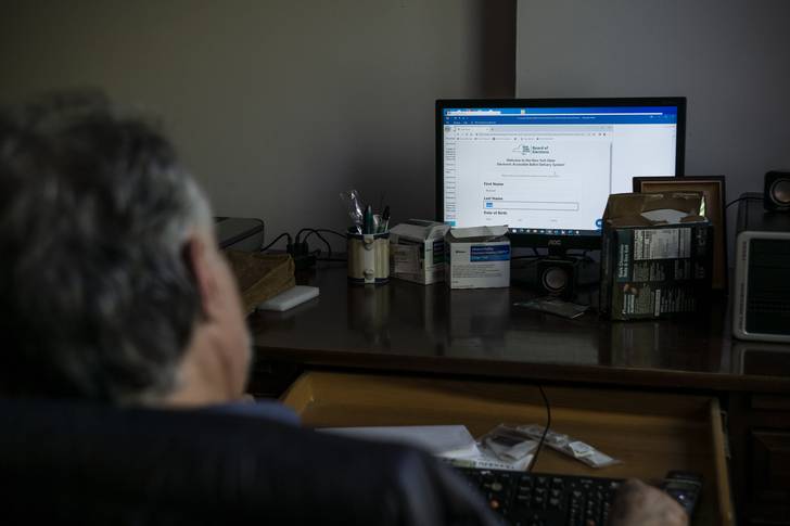 A man sits at his computer, which features an online ballot on the screen.